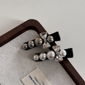 Detailed view of hair clips with grey pearls and rhinestones on a black fabric base