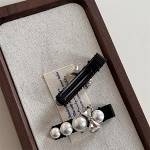 Detailed view of rhinestones bow and pearl hair clips set with black fabric duckbill base