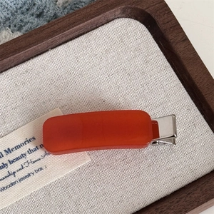 Close-up of orange acetate hair clip with a silver metal base on a beige linen display tray