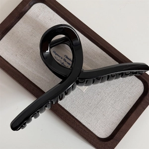 Detail of a 14.5cm glossy black hair claw clip on a wooden tray with elegant text