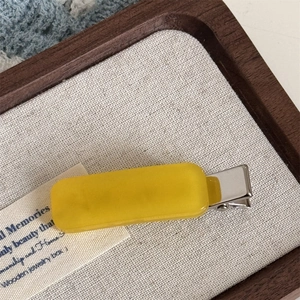 Macro view of bright yellow rectangular resin hair clip with silver metal alligator base