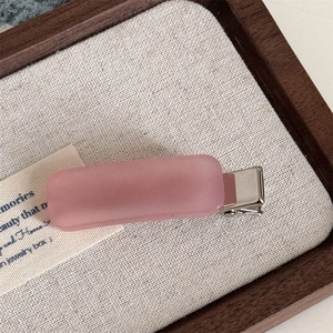 Close-up of pink matte acetate hair clip with silver metal spring on a rustic wooden tray