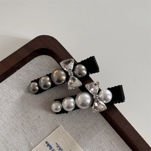 Elegant pearl and rhinestone bow hair clips in grey and white on a wooden tray