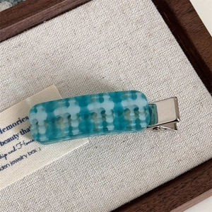 Detailed close-up of blue and green checkered acetate hair clip with silver metal base