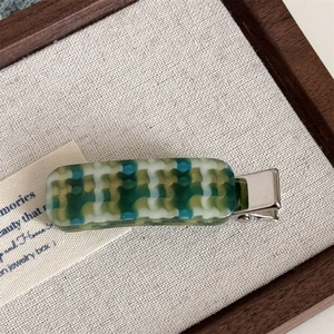 Detailed view of acetate checkered hair clip with green and yellow geometric patterns