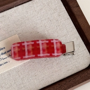 Macro view of a red and pink checkered acetate hair clip with a silver metal duckbill base
