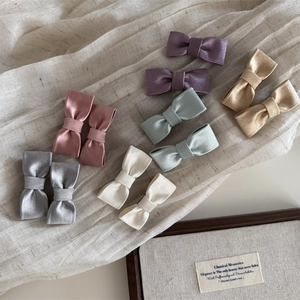 Elegantes Set mit Satin-Schleifen-Haarspangen in Pastellfarben auf Textilhintergrund