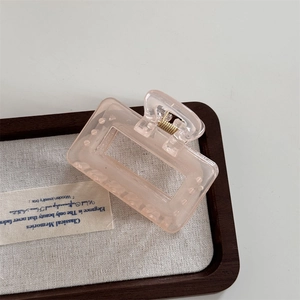 Detailed view of a light pink translucent frosted hollow hair claw clip on a wooden tray