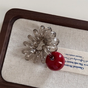 Détail d'un élastique spirale gris avec une perle cerise rouge sur un plateau bois