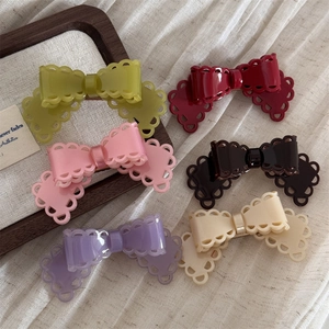 Détail de barrettes papillon ajourées en six couleurs pastel sur un tissu texturé