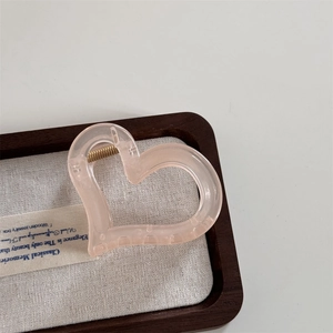 Close-up of translucent pink heart hair claw clip with golden spring on wooden tray