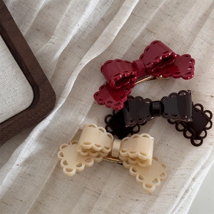 Détail de trois barrettes nœuds évidés en acétate rouge, marron et beige sur tissu