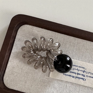 Détail d'un élastique spirale gris foncé avec une perle noire polie sur fond texturé