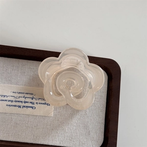 Detailed macro view of a cream-colored camellia flower hair claw clip in a wooden tray