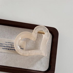 Close-up of translucent beige heart hair claw with a gold metal spring on linen