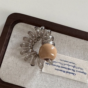 Détail d'un élastique spirale gris avec perle marron dans un coffret à bijoux en bois