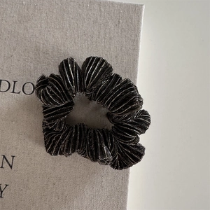 Close-up of black pleated hair tie with silver metallic thread on a textured linen background