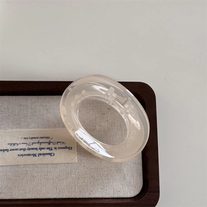 Detail of a translucent beige oval hair claw clip with a glossy finish on a wooden tray