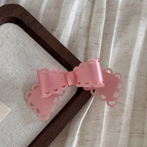Détail d'une pince à cheveux nœud rose avec bords festonnés évidés et texture en résine