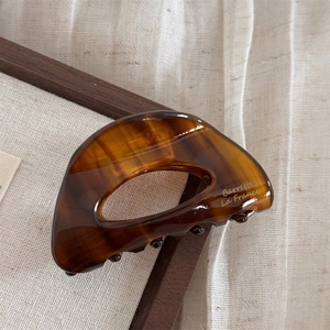 Dettaglio della molletta per capelli in acetato marrone con design cavo e incisione