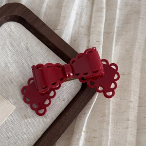 Détail d'une pince à cheveux nœud en acétate rouge foncé avec bords évidés ondulés