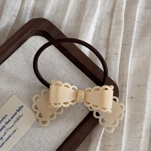 Vue détaillée d'une pince à cheveux papillon crème avec un élastique sur bois