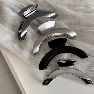 Sleek curved metal hair claws in four premium finishes on a textured fabric surface