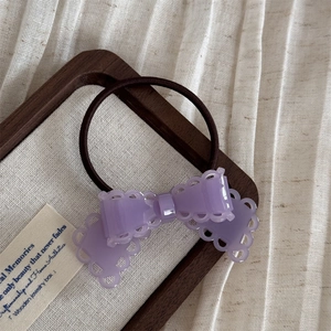 Détail d'un élastique à cheveux nœud violet en acétate avec motif ajouré sur tissu texturé