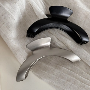 Set of two matte black and champagne silver crescent hair claws on beige linen fabric