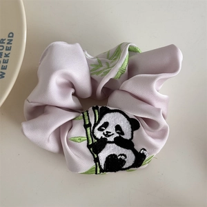 Detail eines rosa Seiden-Scrunchies mit Panda- und Bambus-Stickerei auf weißem Tisch