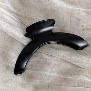Close-up of matte black crescent hair claw clip on soft beige textured fabric