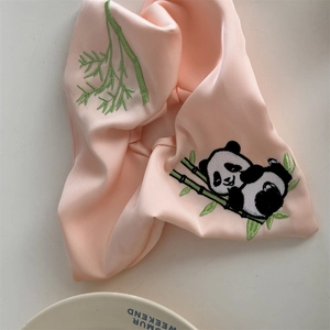 Detail eines rosa Satin-Haargummis mit feiner Stickerei von Pandabär und Bambus