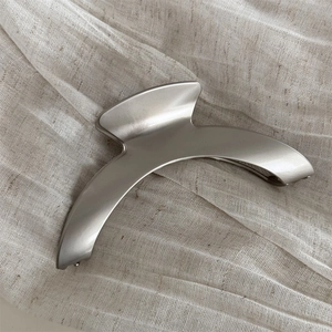 Close-up of matte silver crescent hair claw clip on beige linen texture background