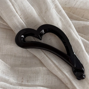 Détail d'une pince banane cœur noire brillante sur un fond en lin texturé