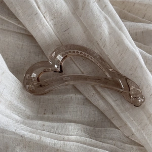 Détail d'une pince à cheveux ambre en forme de cœur sur un tissu beige texturé