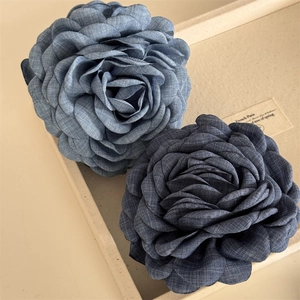 Detail view of light and dark blue denim rose hair clips on a beige fabric tray