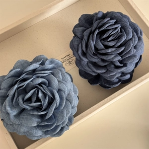 Large denim blue and navy fabric camellia hair claw clips on a beige ceramic tray