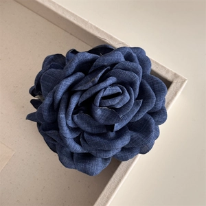 Detail of a large denim blue fabric rose hair claw clip with multi-layered textured petals
