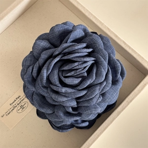 Detail of navy blue denim-textured fabric flower hair clip with multi-layered petals
