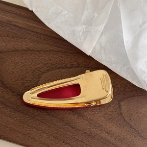 Detail of golden alligator clip with red padding and anti-slip teeth on dark wood