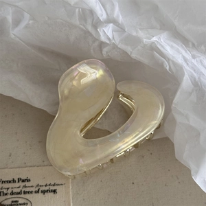 Detailed close-up of a pearlescent cream heart hair claw clip with golden metal teeth