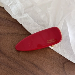 Detailed close-up of handmade red acetate triangle hair clip with golden metal accents