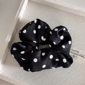 Close-up of black and white polka dot satin scrunchie on a beige fabric display tray