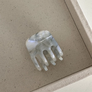 Détail d'une pince à cheveux en acétate marbré gris avec design à cinq dents sur plateau