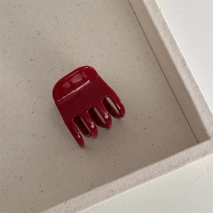Détail d'une pince à cheveux brillante en acétate bordeaux sur un plateau beige