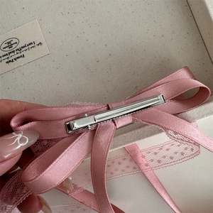 Vue détaillée de la barrette à nœud rose montrant le fermoir en métal et le bord en dentelle