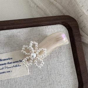Makro-Detail von französischer Acetat-Blumenspange mit Perlen auf einer Schmuckablage aus Holz