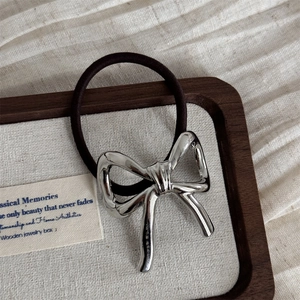 Close-up of a silver polished metal bow hair tie on a luxury wooden jewelry tray