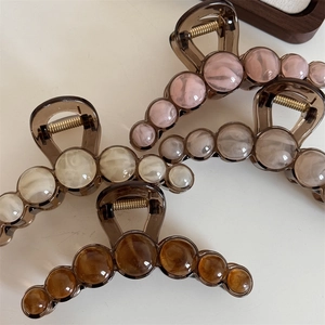 Three elegant marble-textured hair claws in pink, cream, and amber on a neutral background