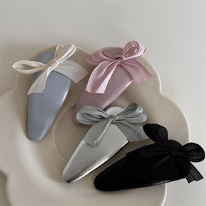 Close-up of four colorful fabric bow hair clips in a white ceramic petal-shaped tray